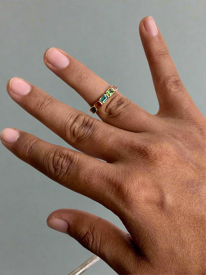 Hand wearing a ring with colored stones on a light background