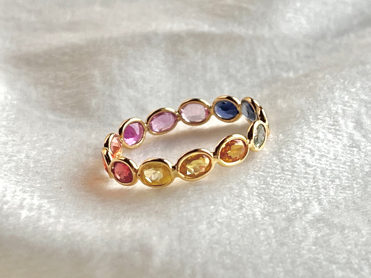 Gold ring with multicolored gemstones on a white fabric background
